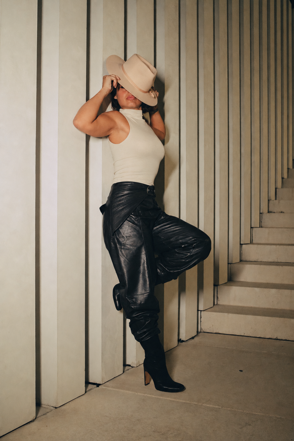 Christina standing beside stone columns with her cream hat brim covering her eyes