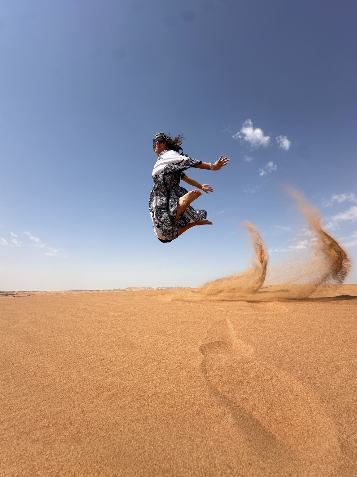 Christina jumping above desert dunes with sand flying behind her
